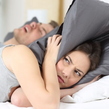 Woman covering ears next to snoring man