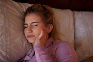 Woman rubbing jaw in pain while lying in bed