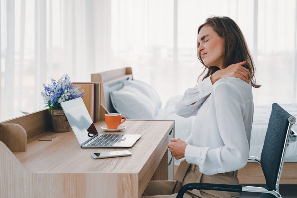 Woman working at desk rubbing neck with eyes closed in pain