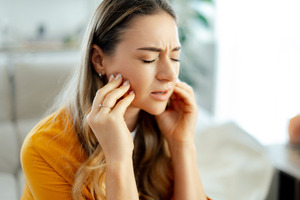 Young woman sitting and rubbing her jaw in pain
