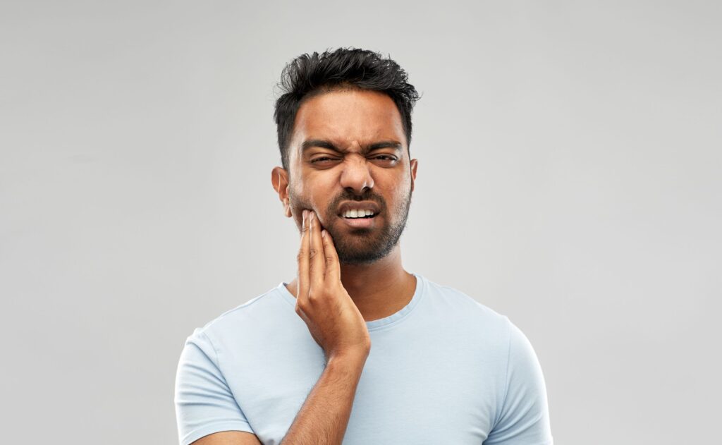 Man squinting in pain and holding hand to sore jaw