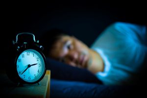 Man in bed awake with alarm clock in foreground
